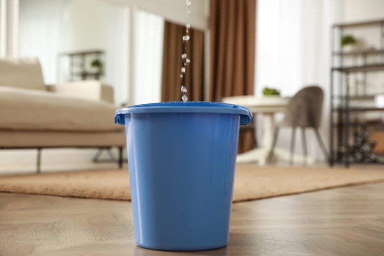 bucket of water on the floor catching water from a roof leak